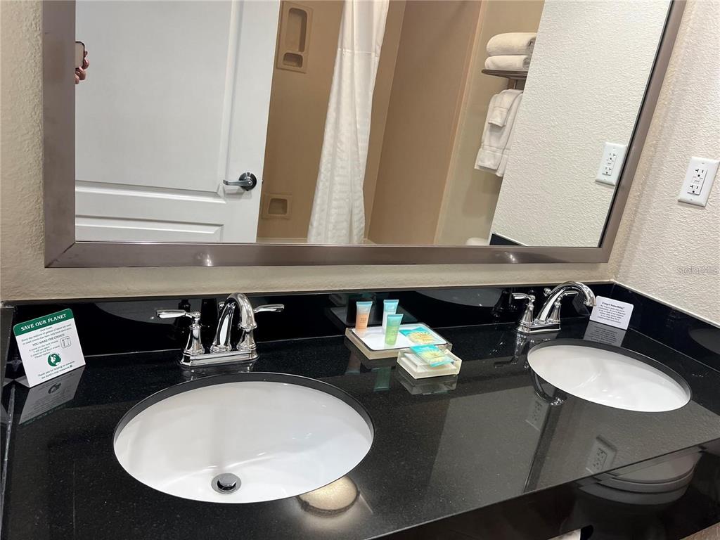 A bathroom vanity features dual sinks, chrome faucets, and a black countertop with a large mirror — 3000 MAINGATE LANE UNIT 218, KISSIMMEE, FL