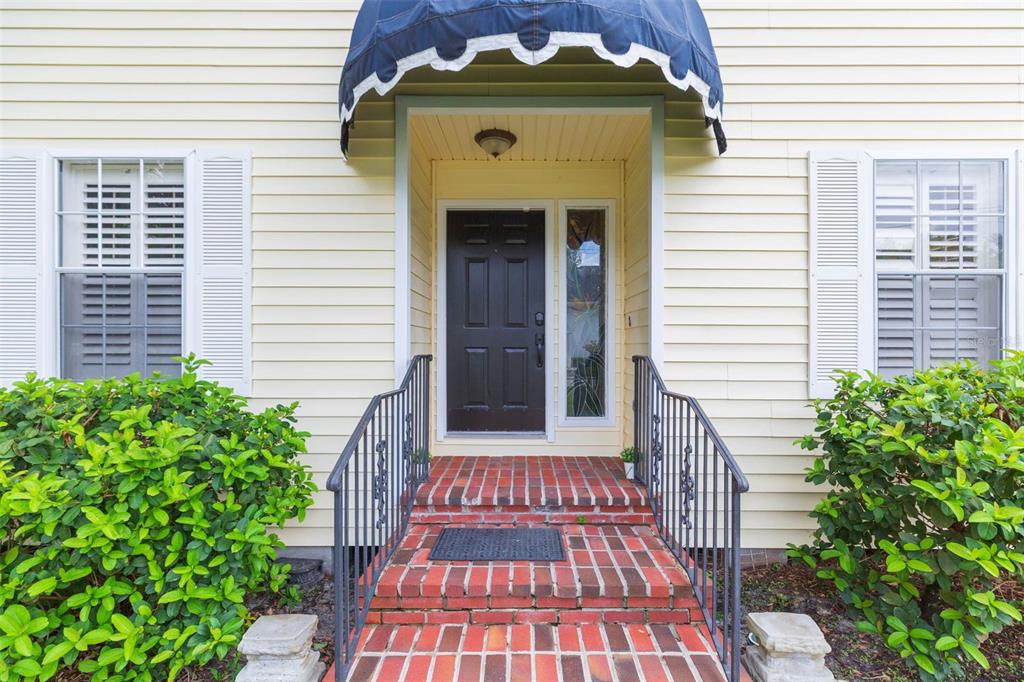 A front entrance with a brick walkway, metal railings, and a dark door under an awning — 4210 W ROLAND STREET, TAMPA, FL