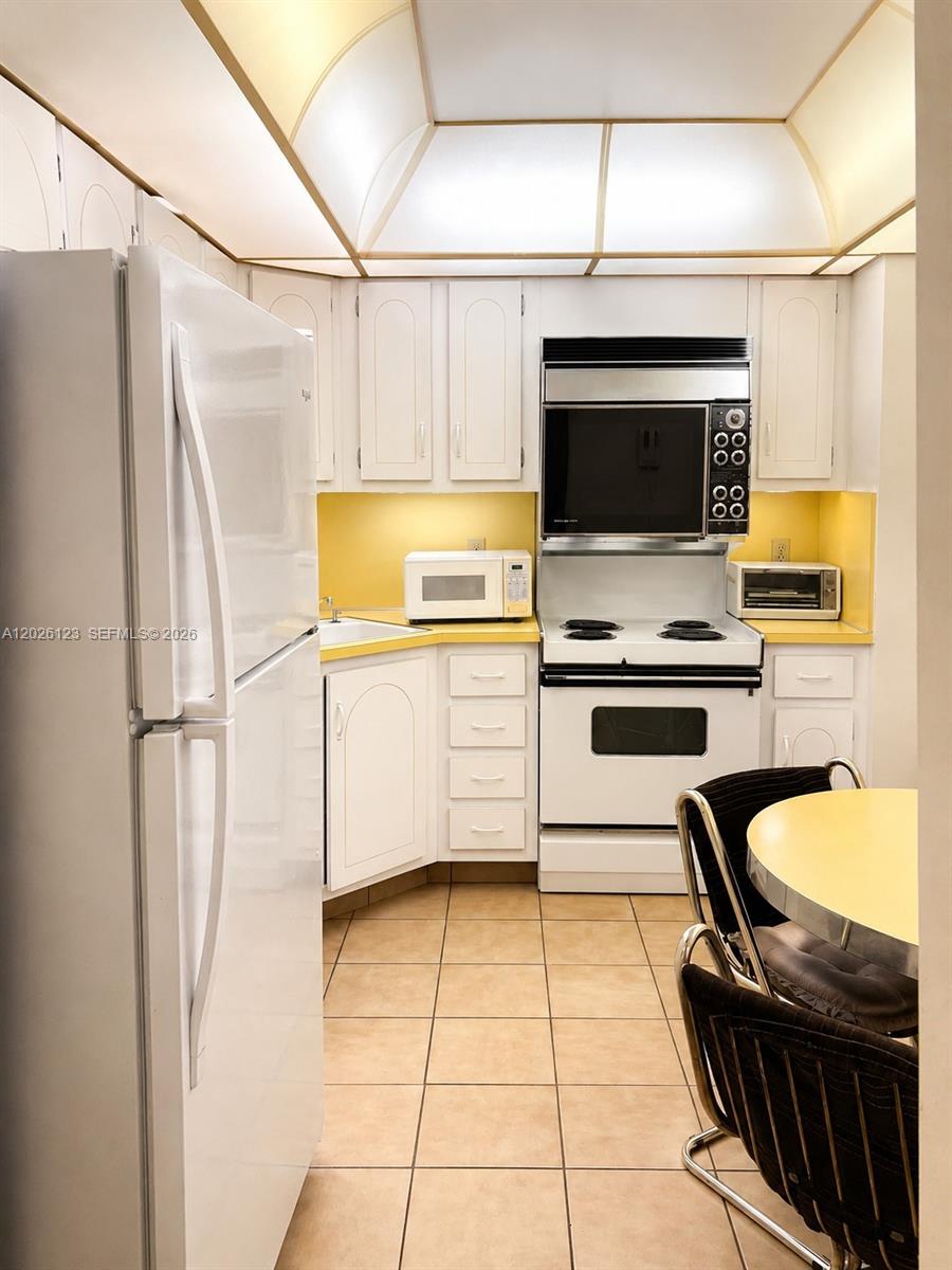 A kitchen features white cabinets, yellow countertops, a white refrigerator, and a tiled floor — 1865 S Ocean Dr # 2G, Hallandale Beach FL 33009, HALLANDALE BEACH, FL