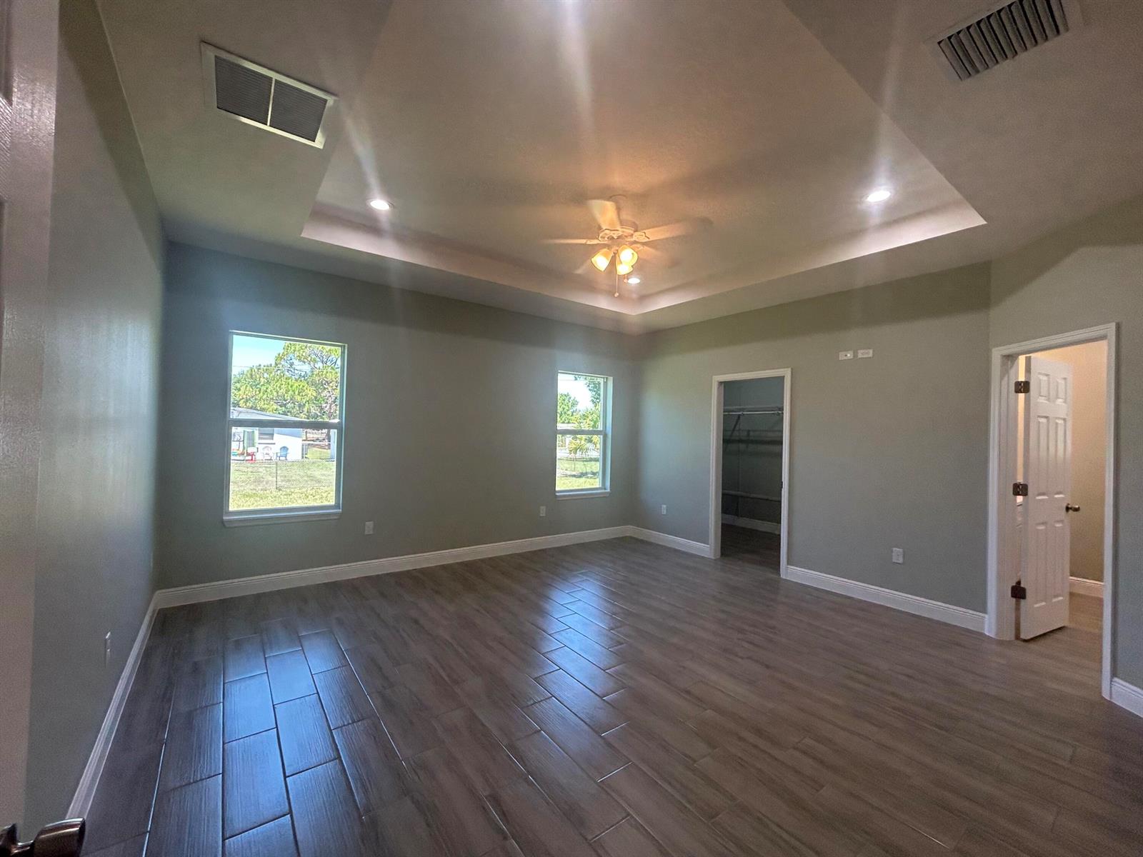 A bedroom with a tray ceiling, ceiling fan, wood-look tile flooring, and two windows — 3935 NW 18th Avenue, Okeechobee FL 34972, OKEECHOBEE, FL