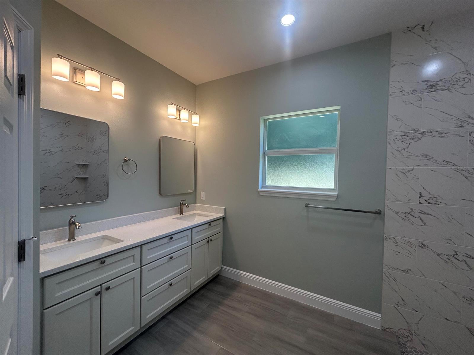 A bathroom features a double vanity with white cabinets, marble-look mirrors, and tiled shower walls — 3935 NW 18th Avenue, Okeechobee FL 34972, OKEECHOBEE, FL