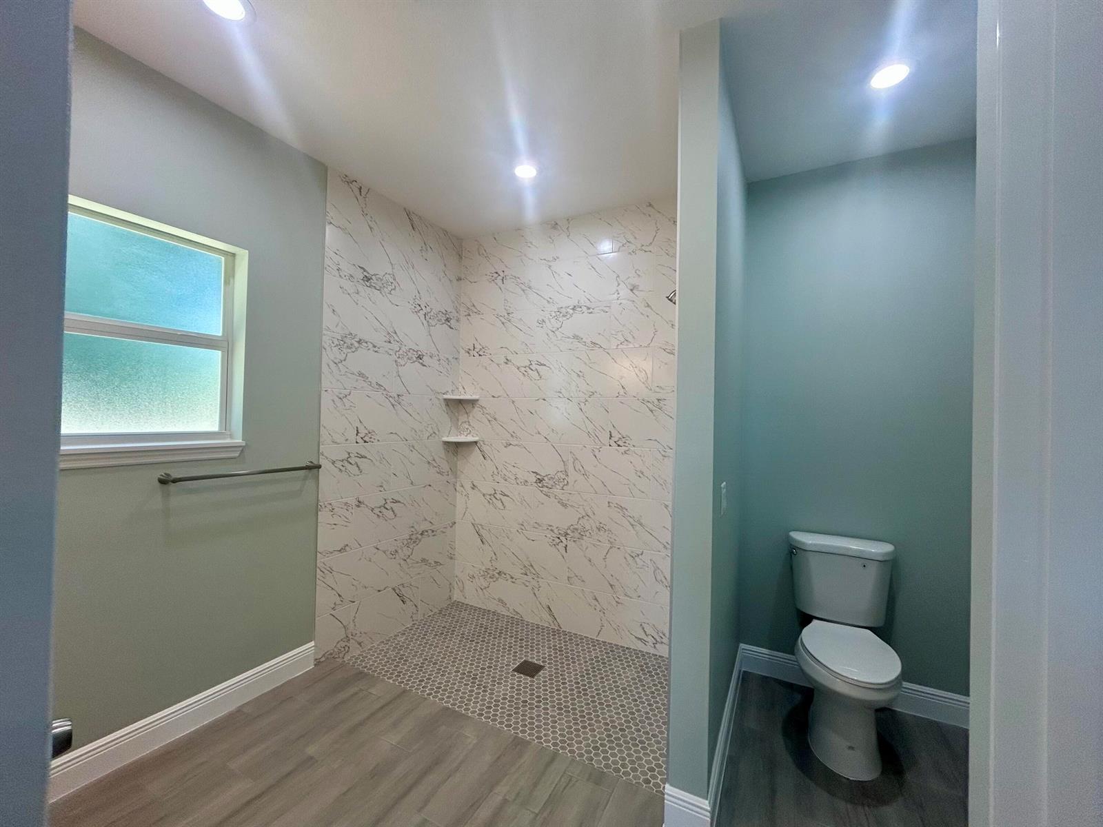A bathroom features a walk-in shower with marble-look tile, a toilet nook, and wood-look flooring — 3935 NW 18th Avenue, Okeechobee FL 34972, OKEECHOBEE, FL
