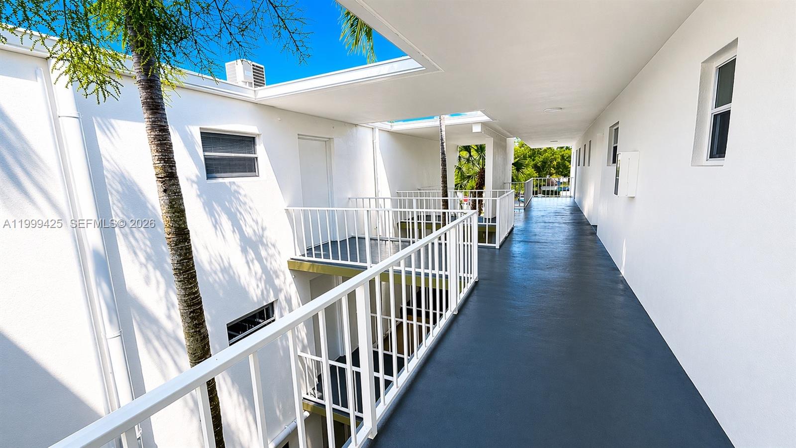 An outdoor walkway with white railings overlooks a lower level with palm trees — 4255 N University Dr # 308, Sunrise FL 33351, SUNRISE, FL