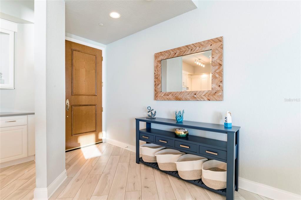 An entryway features a dark blue console table, a wood-framed mirror, and light wood flooring — 1170 GULF BOULEVARD UNIT 2203, CLEARWATER BEACH, FL