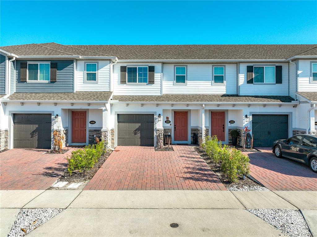 A row of three-story townhouses features brick driveways, dark garage doors, and red front doors — 4460 CAMPSITE LOOP, ORLANDO, FL