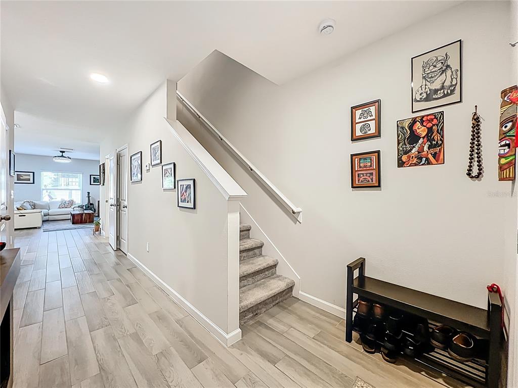 A hallway features wood-look tile flooring, a carpeted staircase, and a shoe rack — 4460 CAMPSITE LOOP, ORLANDO, FL