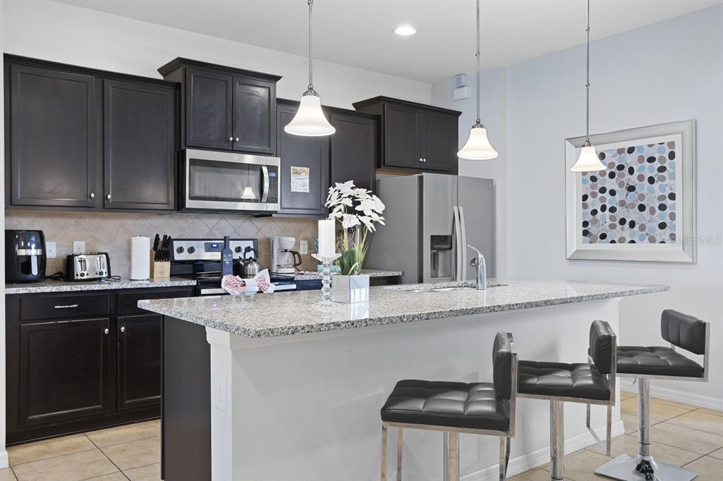 A kitchen features dark wood cabinets, granite countertops, a center island, and two bar stools — 1724 LIMA AVE, KISSIMMEE, FL