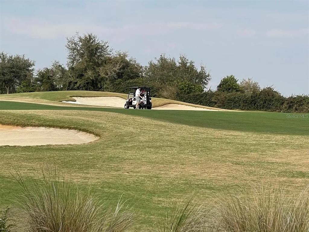A golf cart sits on a green fairway near sand bunkers and trees — 811 OCEAN COURSE AVENUE UNIT 811, DAVENPORT, FL