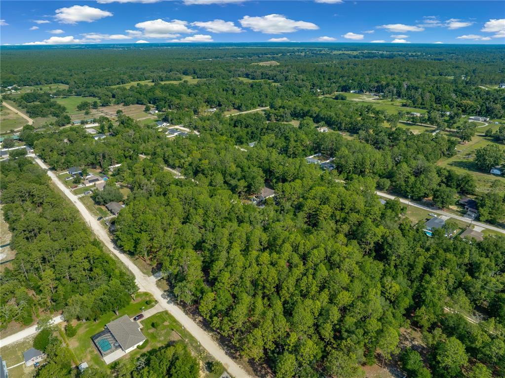 An aerial view shows a rural residential area with houses scattered among dense green trees — SW 18TH PLACE, OCALA, FL