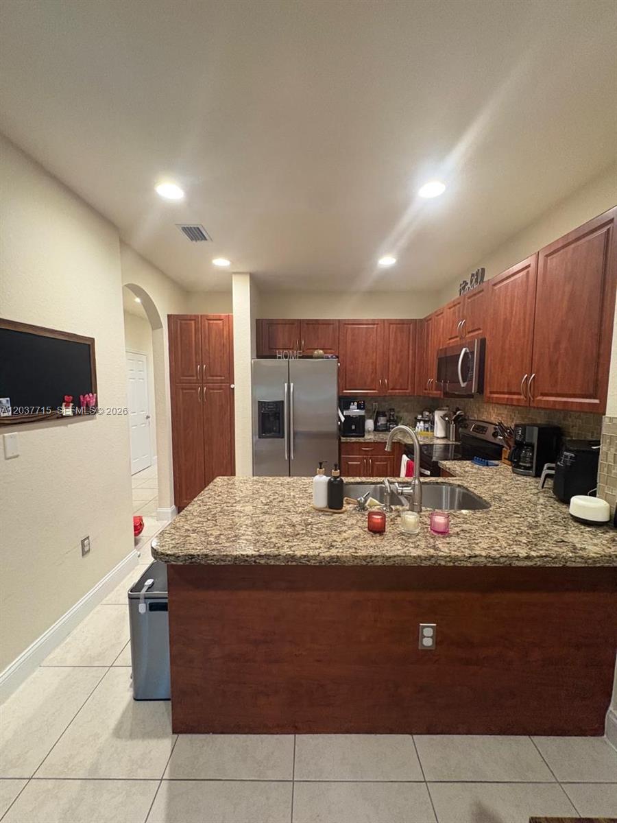 A kitchen features wood cabinets, granite countertops, a stainless steel refrigerator, and tile flooring — 280 Las Brisas Cir # 280, Sunrise FL 33326, SUNRISE, FL