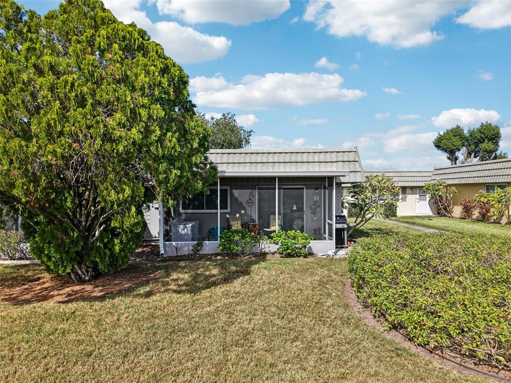 A single-story home with a screened-in porch, a large tree, and a manicured lawn — 201 KINGS BOULEVARD UNIT 13, SUN CITY CENTER, FL