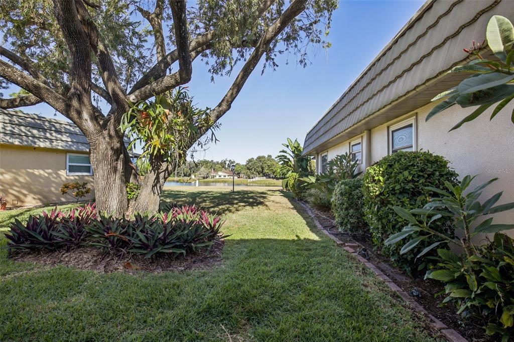 A view of a grassy backyard between two buildings with a pond in the distance — 201 KINGS BOULEVARD UNIT 13, SUN CITY CENTER, FL