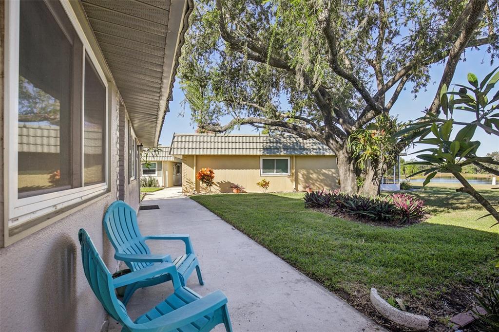 A concrete walkway leads past a house exterior with two blue chairs and landscaping — 201 KINGS BOULEVARD UNIT 13, SUN CITY CENTER, FL
