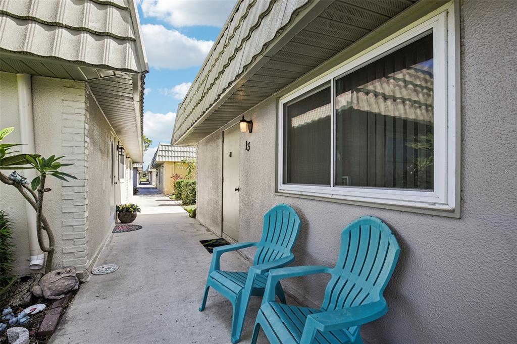 Two turquoise chairs sit on a concrete walkway outside a unit with a numbered door — 201 KINGS BOULEVARD UNIT 13, SUN CITY CENTER, FL