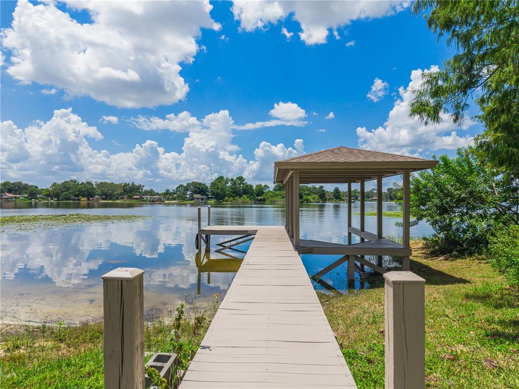 A wooden dock with a covered boat slip extends into a calm lake under blue skies — 430 BYWATER DRIVE, ORLANDO, FL
