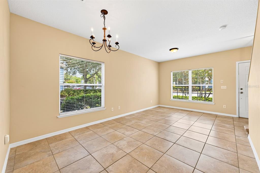 An empty room features beige walls, large square floor tiles, and a black chandelier — 102 WILTON CIRCLE, SANFORD, FL