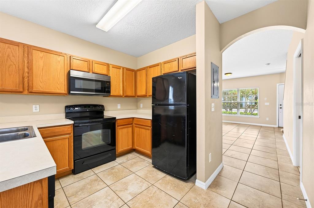A kitchen with oak cabinets, black appliances, and tile flooring leads into an adjacent room — 102 WILTON CIRCLE, SANFORD, FL