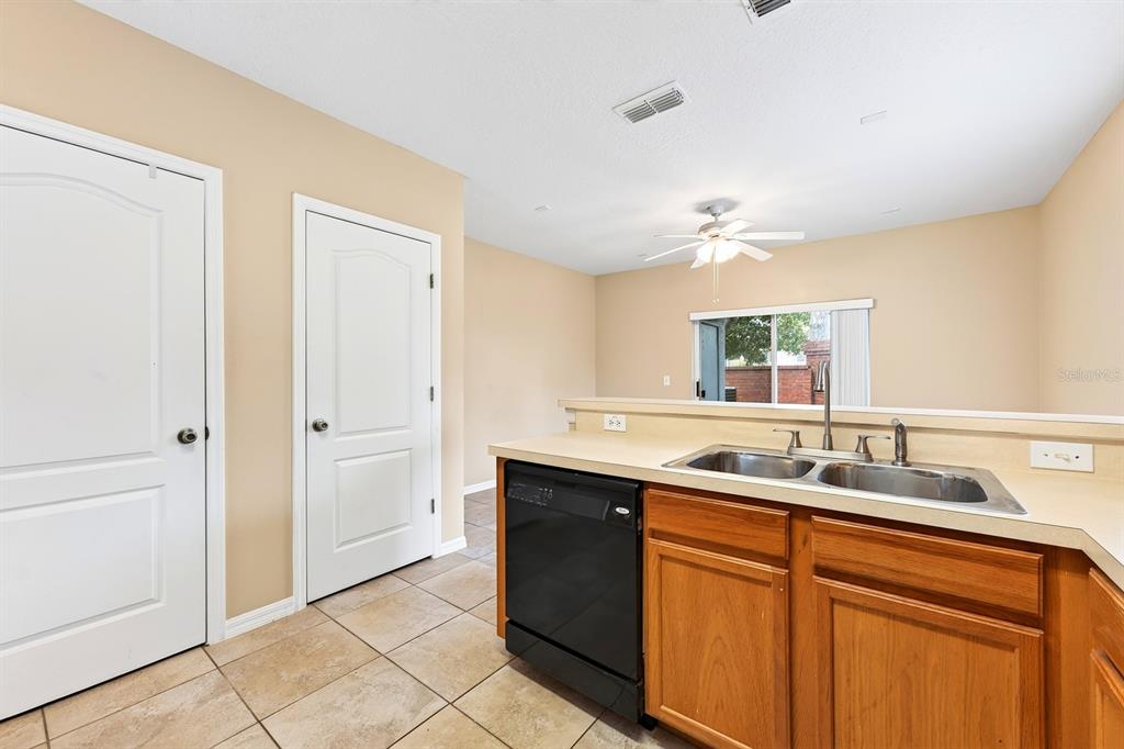 A kitchen with wood cabinets, a black dishwasher, and tile flooring overlooks an adjacent room — 102 WILTON CIRCLE, SANFORD, FL