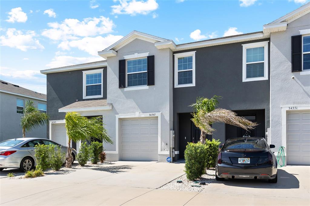 A row of two-story townhouses with gray and white stucco exteriors and attached garages — 34347 SORREL MINT DRIVE, WESLEY CHAPEL, FL