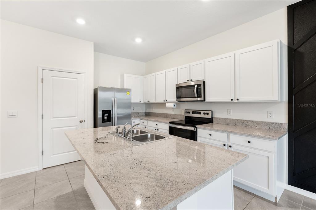 A kitchen features white cabinets, granite countertops, a central island, and stainless steel appliances — 34347 SORREL MINT DRIVE, WESLEY CHAPEL, FL