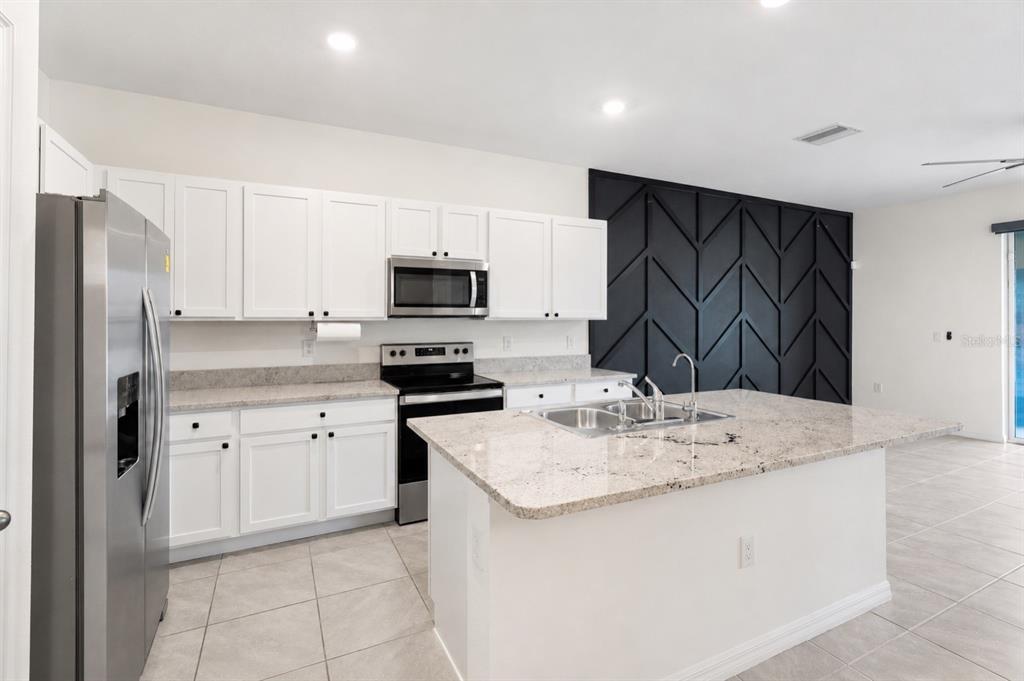 A kitchen with white cabinets, granite countertops, stainless steel appliances, and a black accent wall — 34347 SORREL MINT DRIVE, WESLEY CHAPEL, FL