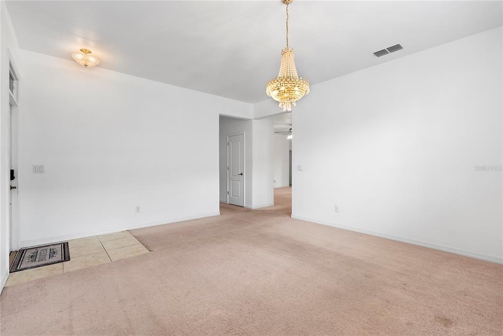 A carpeted room features a crystal chandelier, white walls, and a small tiled entryway — 2336 CROSSTON CIRCLE, ORLANDO, FL