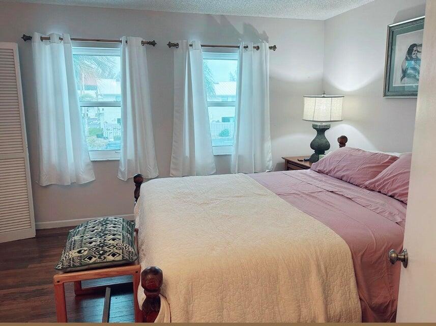 A bedroom features a bed with pink bedding, a cream quilt, and two windows with curtains — 9417 S Ocean Drive # 37, Jensen Beach FL 34957, JENSEN BEACH, FL