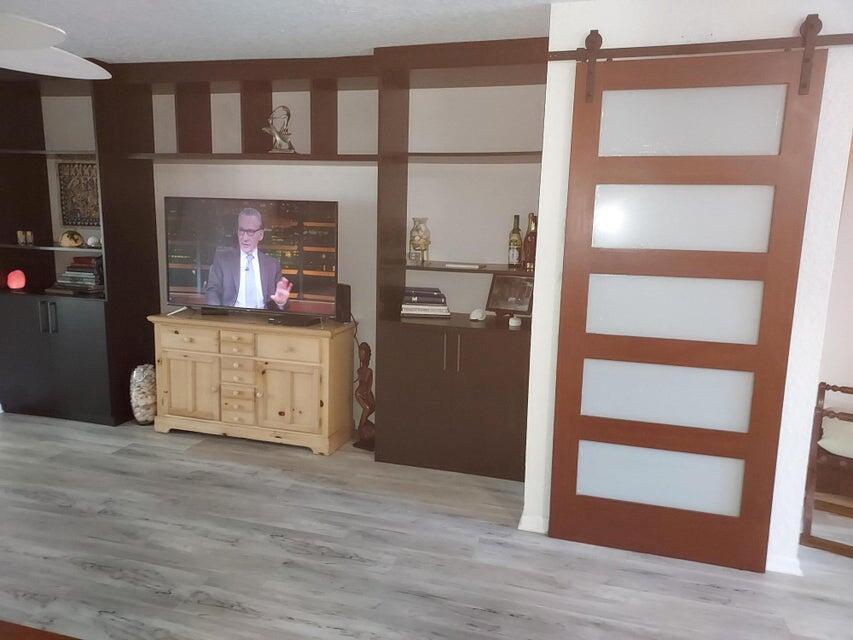 A living room features built-in dark wood shelving, a light wood media console, and a sliding door — 9417 S Ocean Drive # 37, Jensen Beach FL 34957, JENSEN BEACH, FL