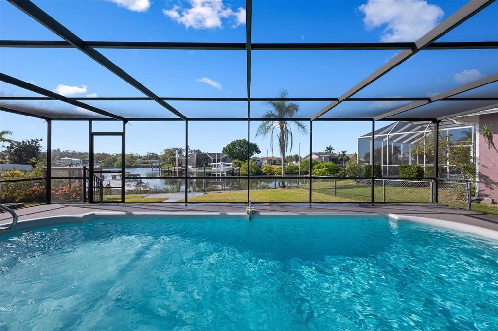 A swimming pool sits inside a screened-in lanai overlooking a canal with docked boats — 1503 MARLIN STREET, NOKOMIS, FL