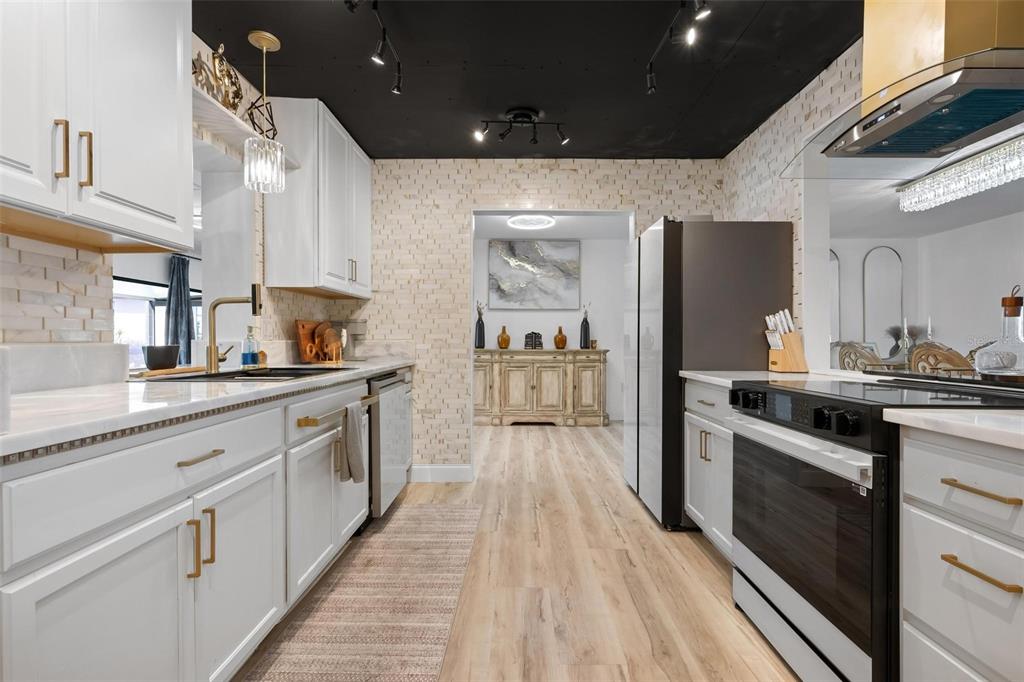 A kitchen features white cabinets, gold hardware, a black ceiling, and light wood-look flooring — 1503 MARLIN STREET, NOKOMIS, FL