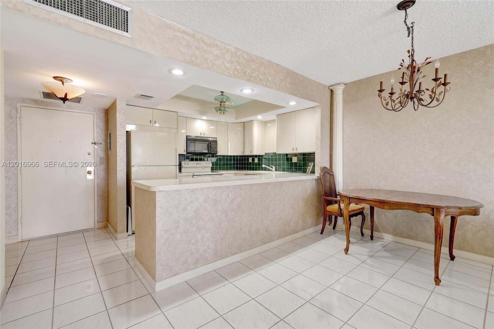 A kitchen with a breakfast bar and dining area features white tile flooring and cabinets — 500 Three Islands Blvd # 622, Hallandale Beach FL 33009, HALLANDALE BEACH, FL