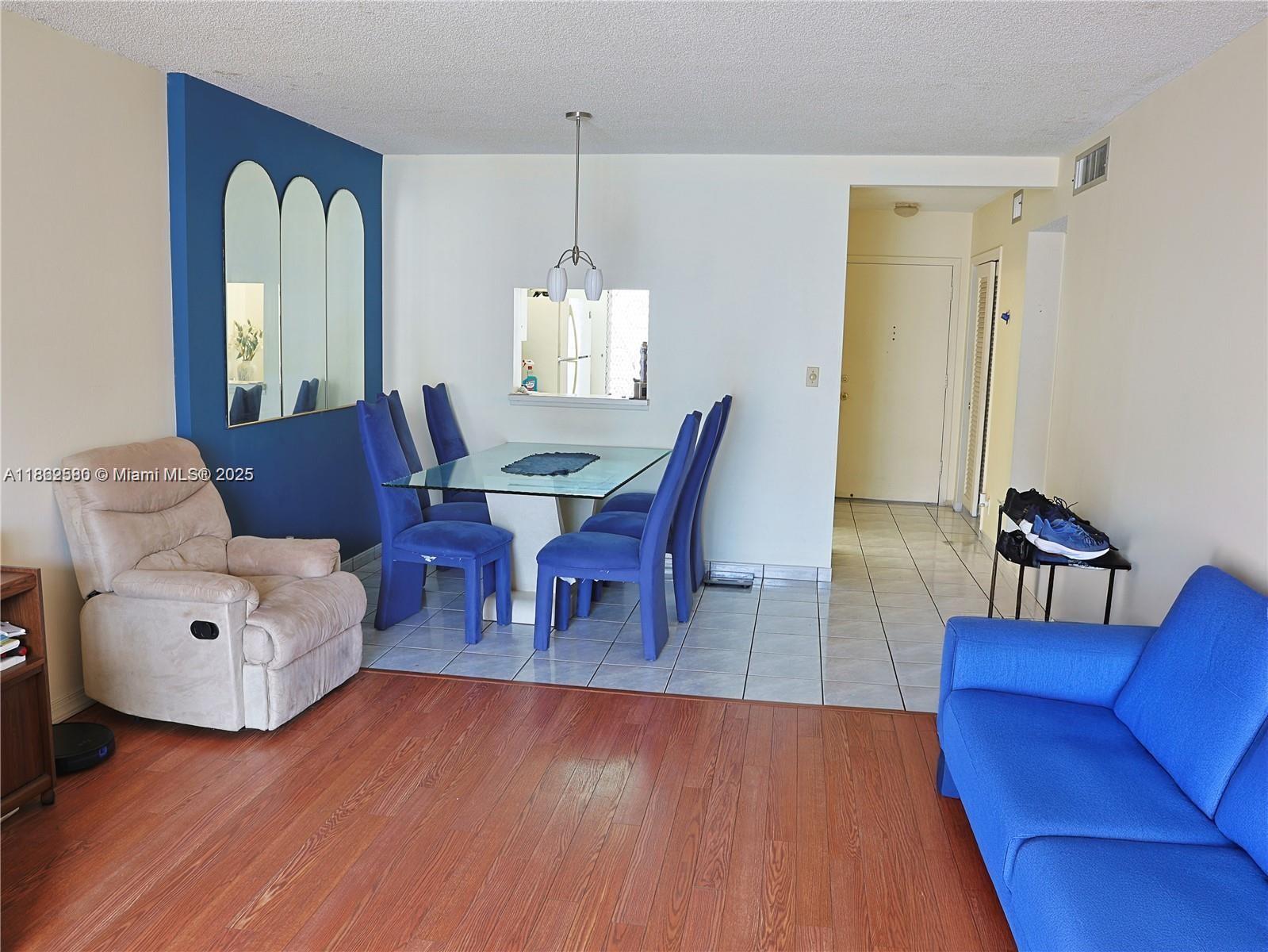 A dining area with a glass table and blue chairs sits beside a living room — 319 NE 14th Ave # 505, Hallandale Beach FL 33009, HALLANDALE BEACH, FL