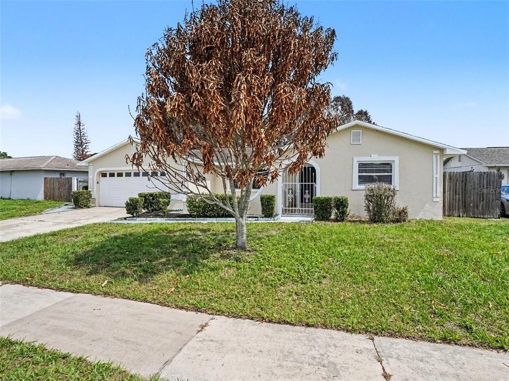 A single-story house with a beige exterior, a two-car garage, and a large brown tree — 615 THOMAS JEFFERSON WAY, ORLANDO, FL