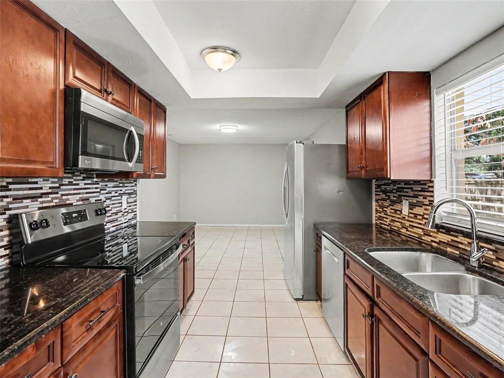A galley kitchen features dark wood cabinets, granite countertops, stainless steel appliances, and tiled floors — 615 THOMAS JEFFERSON WAY, ORLANDO, FL