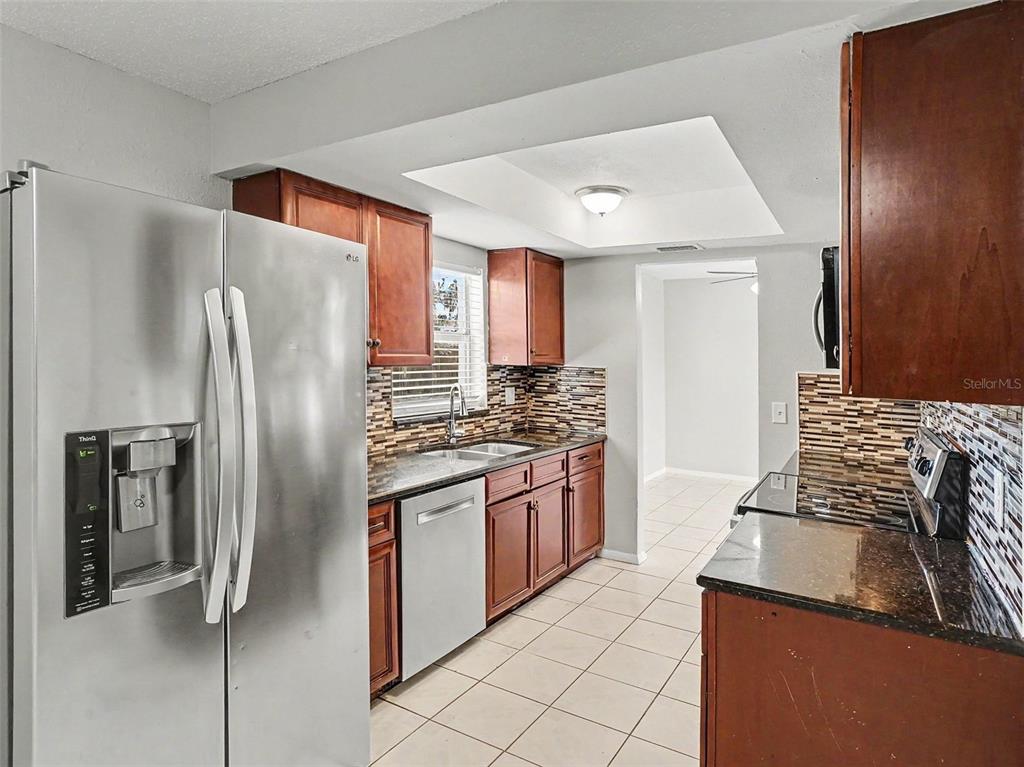 A kitchen features stainless steel appliances, dark wood cabinets, granite countertops, and a tiled backsplash — 615 THOMAS JEFFERSON WAY, ORLANDO, FL