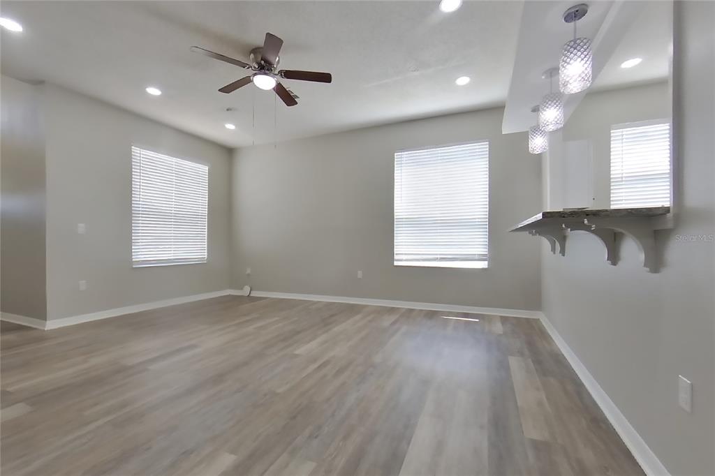 An empty living room features light-colored wood-look flooring, a ceiling fan, and a breakfast bar — 408 E IDLEWILD AVENUE, EUSTIS, FL