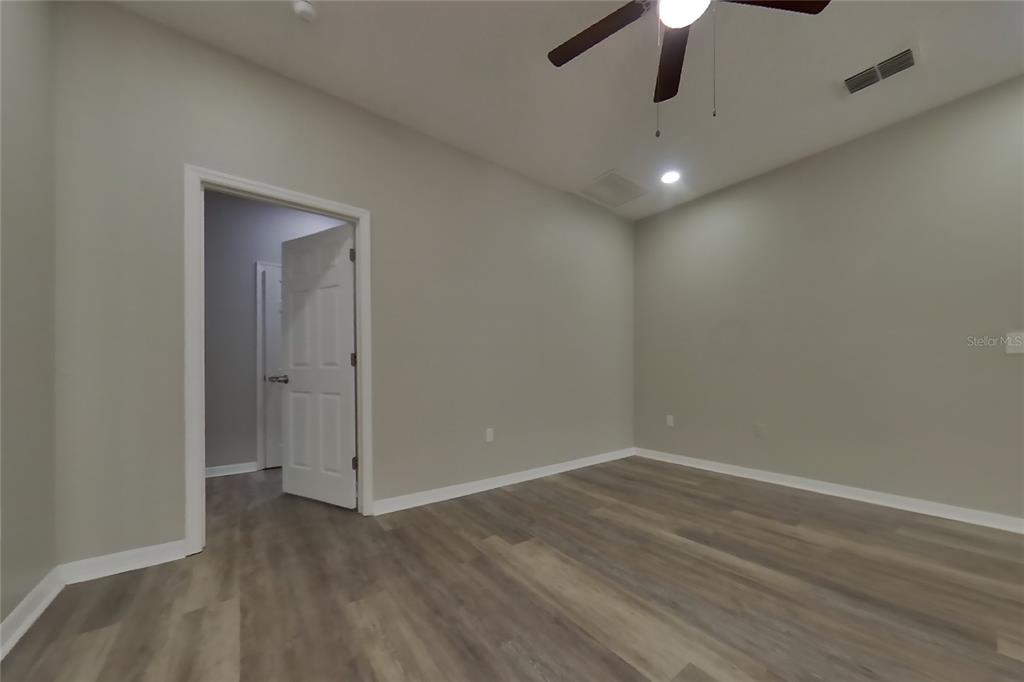A bedroom with light gray walls, wood-look flooring, a ceiling fan, and an open doorway — 408 E IDLEWILD AVENUE, EUSTIS, FL
