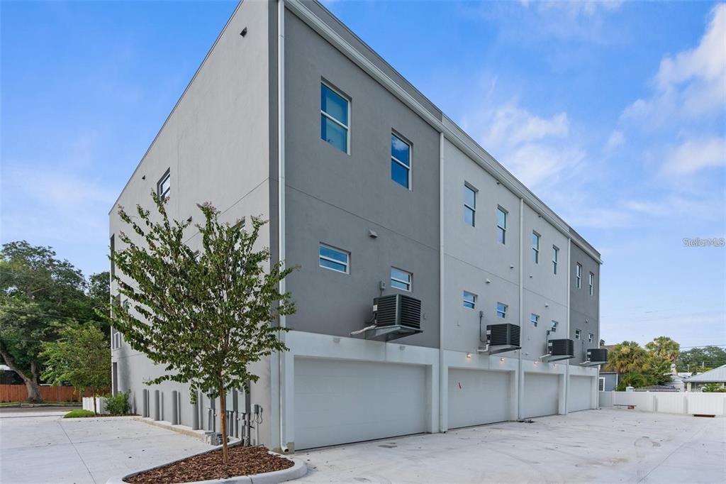 A multi-story grey townhouse building features multiple garage doors and exterior air conditioning units — 102 W ADALEE STREET UNIT 3, TAMPA, FL