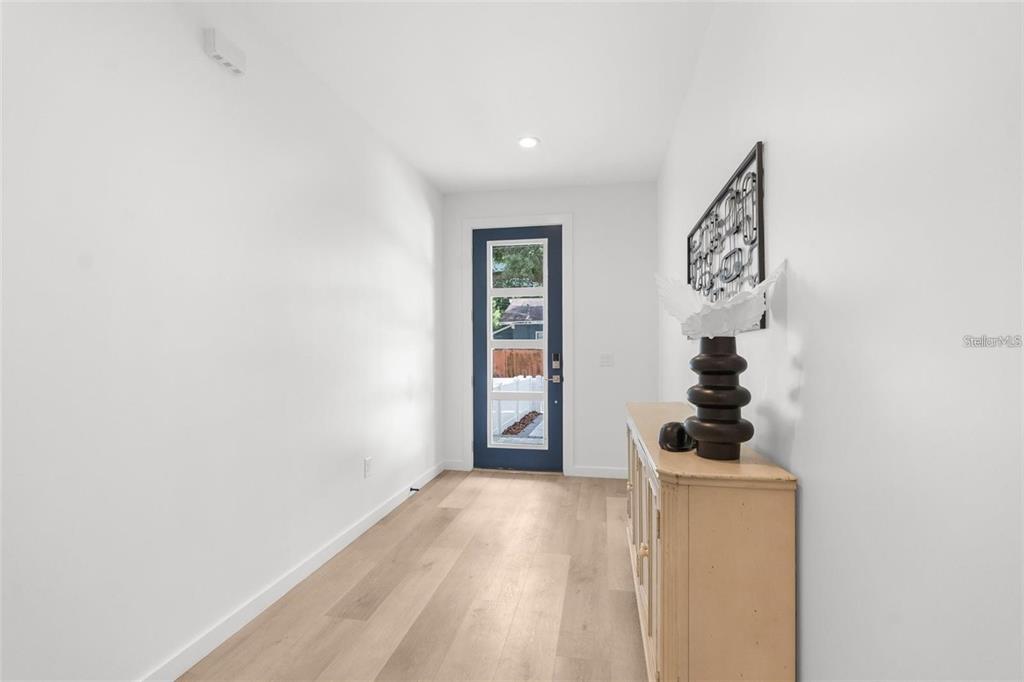 A bright entryway features light wood-look flooring, white walls, and a dark blue front door — 102 W ADALEE STREET UNIT 3, TAMPA, FL
