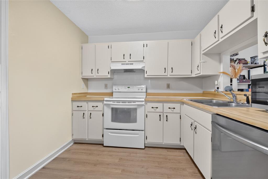 A kitchen with white cabinets, light wood countertops, a white stove, and wood-look flooring — 2701 NE 10TH STREET UNIT 603, OCALA, FL