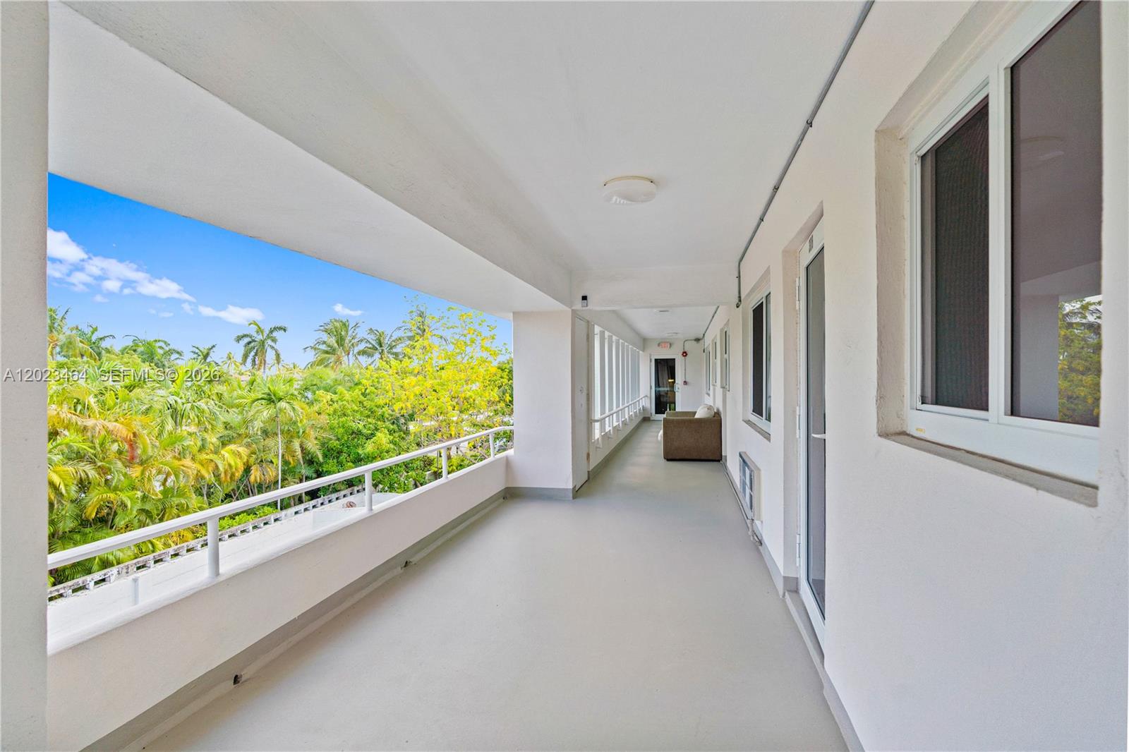 An outdoor balcony features a white railing, concrete flooring, and views of lush tropical trees — 10190 Collins Ave, Bal Harbour FL 33154, BAL HARBOUR, FL