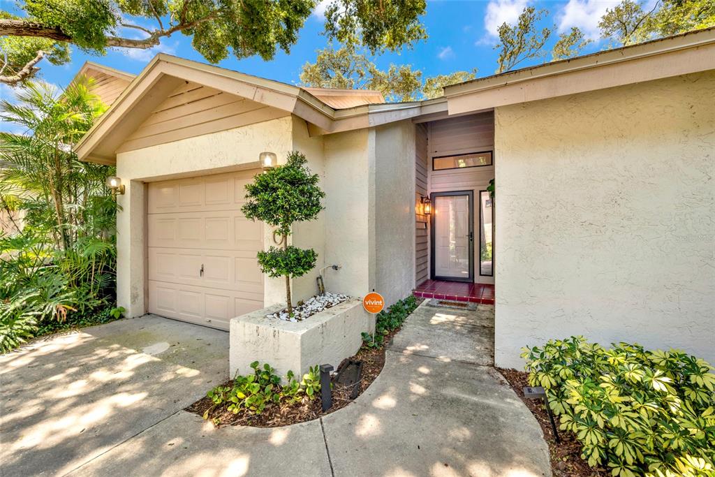 The exterior of a single-story home features a garage, a front entryway, and landscaping — 1900 WHISPERING WAY, TARPON SPRINGS, FL