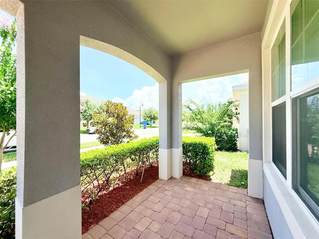 A covered porch features light-colored pavers, gray stucco columns, and a view of landscaping — 2993 NOTTEL DRIVE, ST CLOUD, FL