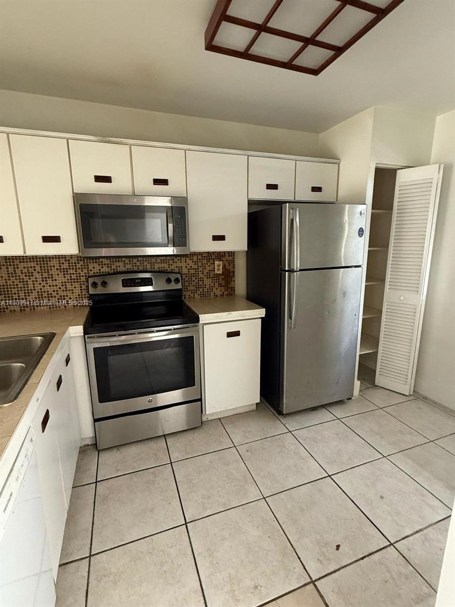 A kitchen features white cabinets, stainless steel appliances, a tiled backsplash, and light floor tiles — 438 NE 210th Cir Ter # 4B, Miami FL 33179, MIAMI, FL