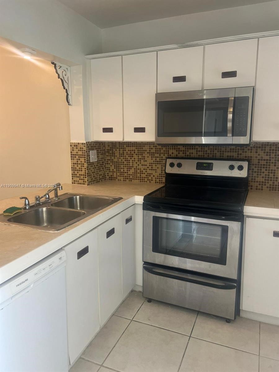 A kitchen features white cabinets, stainless steel appliances, and a brown mosaic tile backsplash — 438 NE 210th Cir Ter # 4B, Miami FL 33179, MIAMI, FL