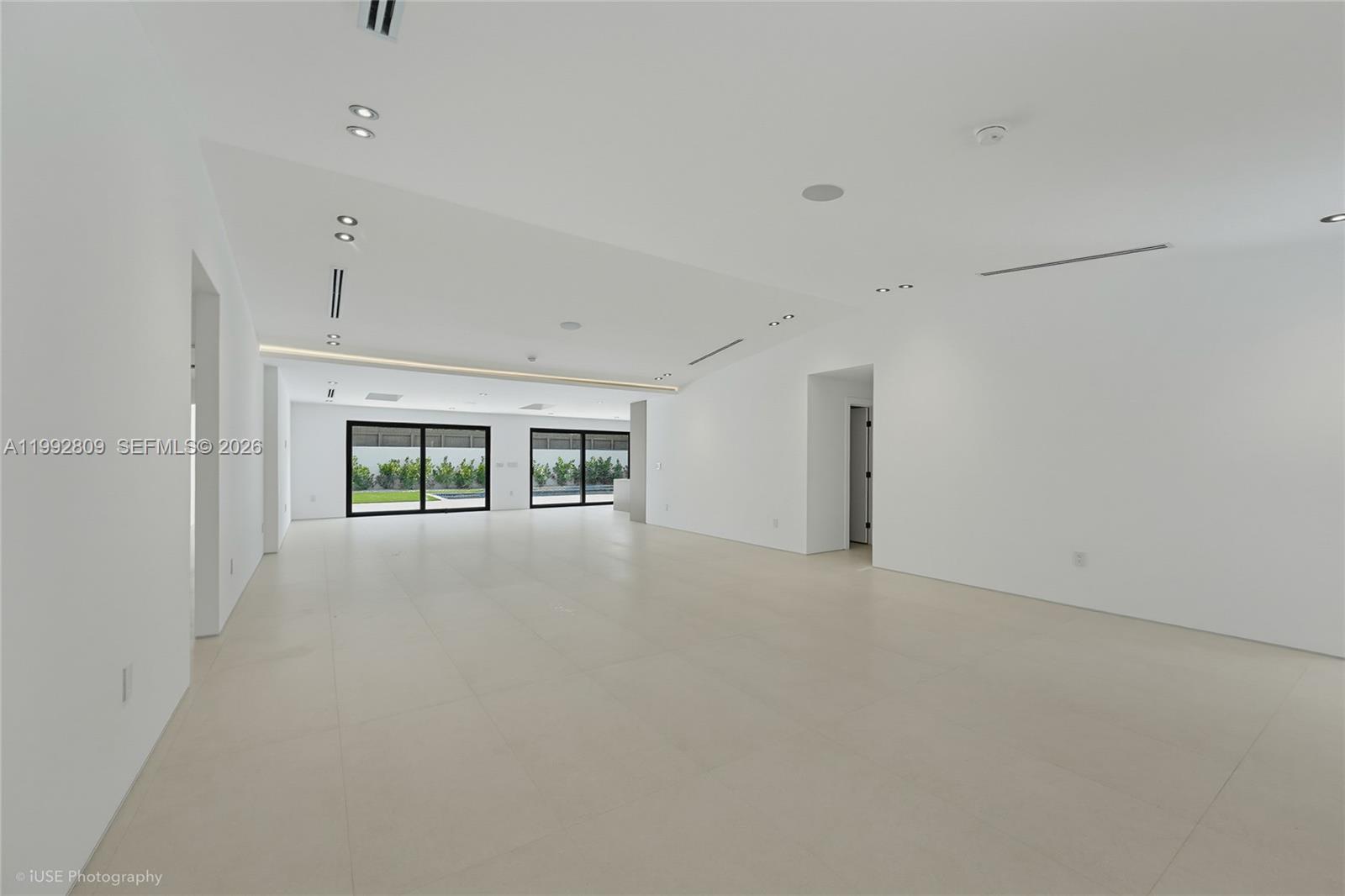 A spacious, minimalist room features white walls, large tile flooring, and sliding glass doors — 21490 Highland Lakes Blvd, Miami FL 33179, MIAMI, FL