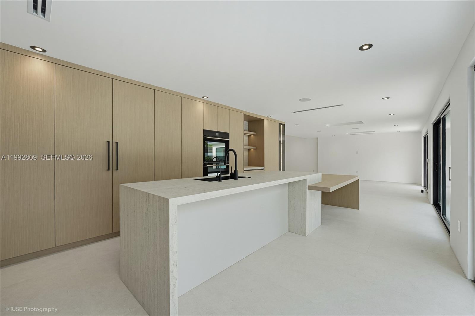 A modern kitchen features light wood cabinetry, a stone waterfall island, and white tile flooring — 21490 Highland Lakes Blvd, Miami FL 33179, MIAMI, FL