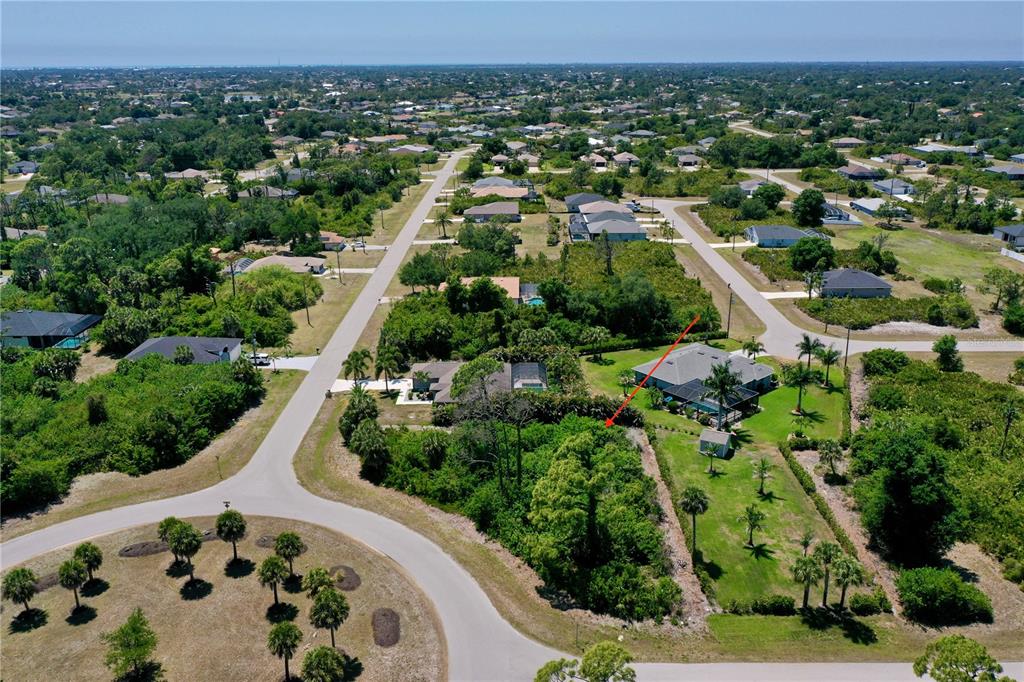 An aerial view shows a residential neighborhood with a red arrow pointing toward a wooded lot — 125 AUSTRALIAN DRIVE, ROTONDA WEST, FL