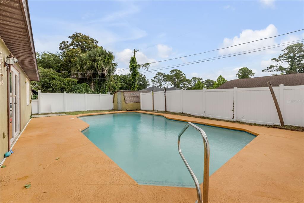 A backyard features an in-ground swimming pool surrounded by a tan deck and white fencing — 2509 WOODLAND DRIVE, EDGEWATER, FL