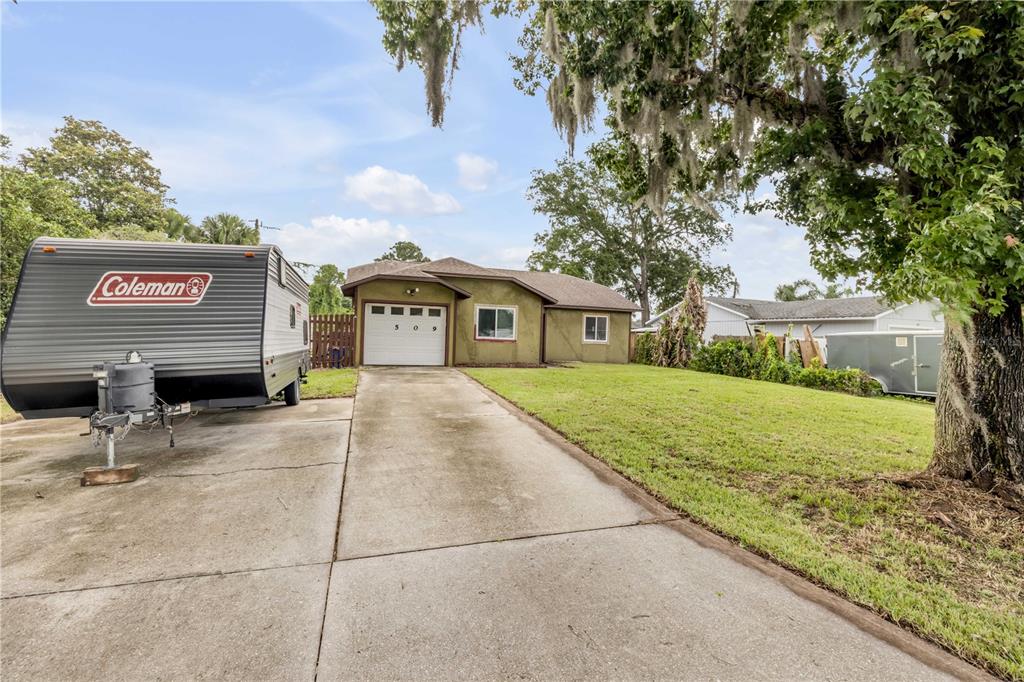 A single-story house with a concrete driveway and a parked travel trailer in the foreground — 2509 WOODLAND DRIVE, EDGEWATER, FL
